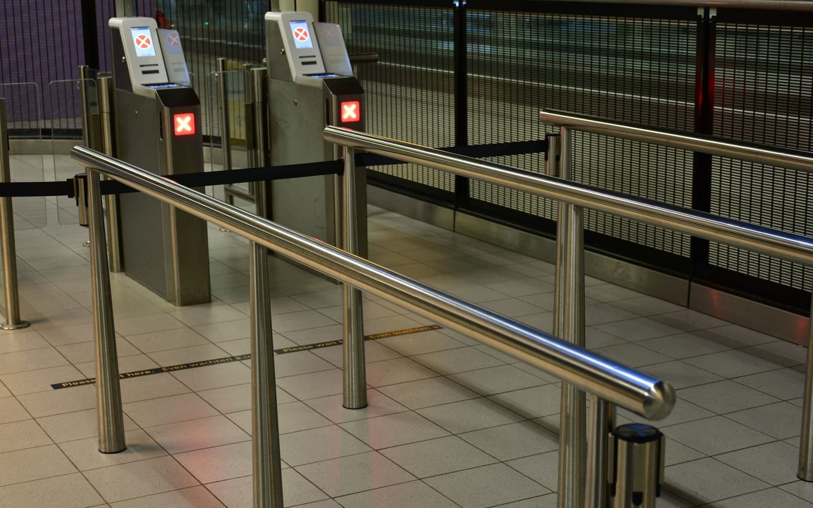 A row of automated access control barriers with card readers on their pedestals, closed across a walkway
