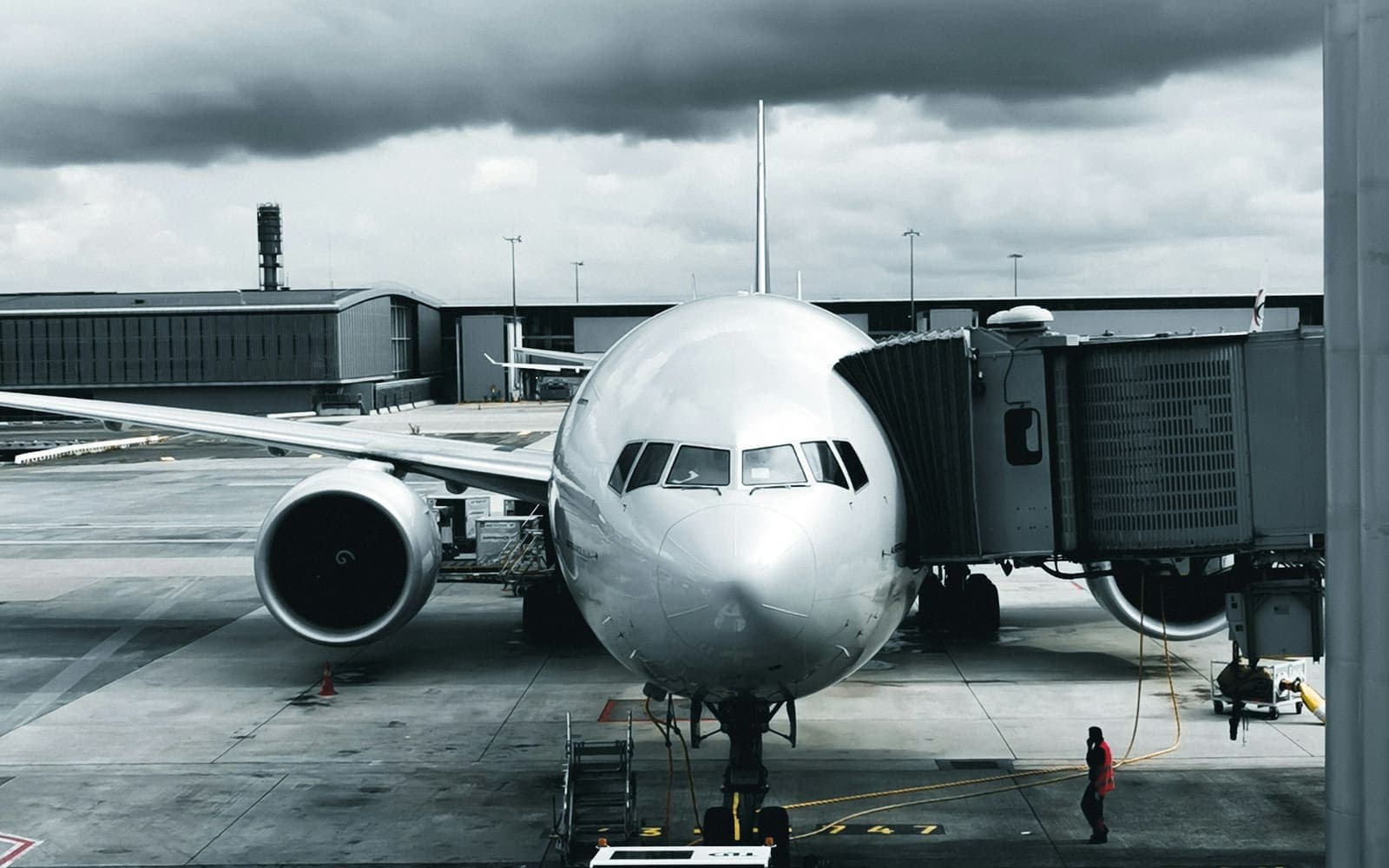 An airliner parked nose on at a stand with its passenger boarding bridge attached and a tug in front of it, under heavy cloud