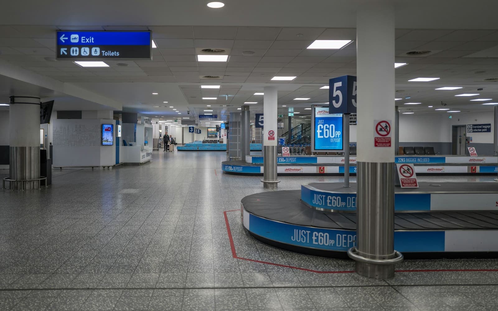 A baggage reclaim hall with two carousels and their conveyor runs, seen from the concourse floor