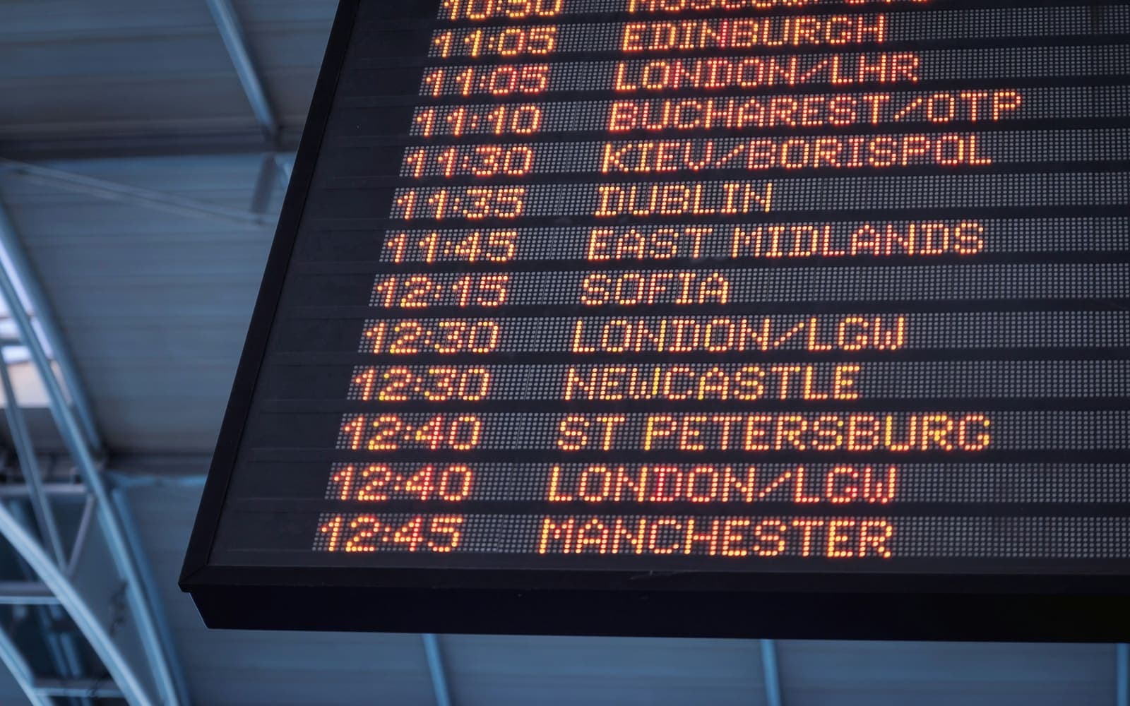 A flight information display board listing departure times and destinations in amber type