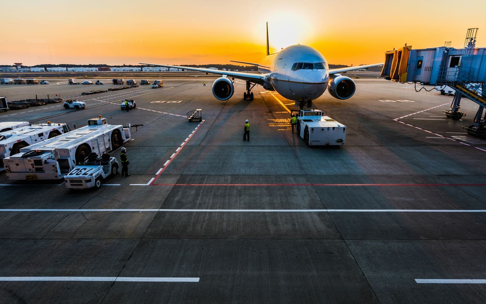 An airliner on stand at sunrise surrounded by ground support equipment, with a loader and tugs alongside it