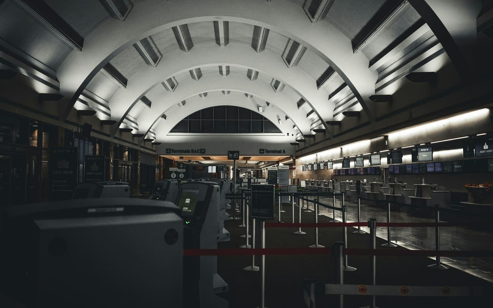 A terminal check in hall under a ribbed vaulted roof, its counters and queue lanes empty
