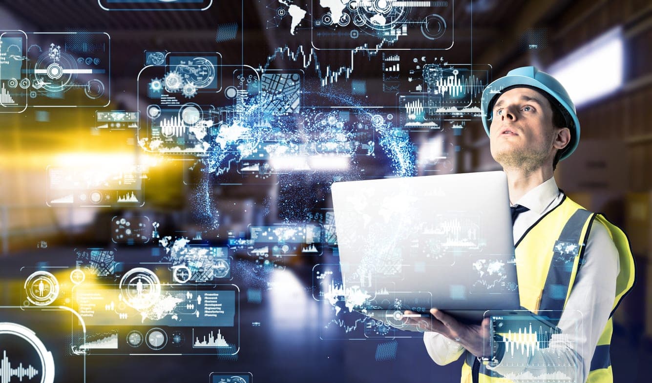An engineer in a hard hat holding a laptop, surrounded by data overlays representing research and analysis.