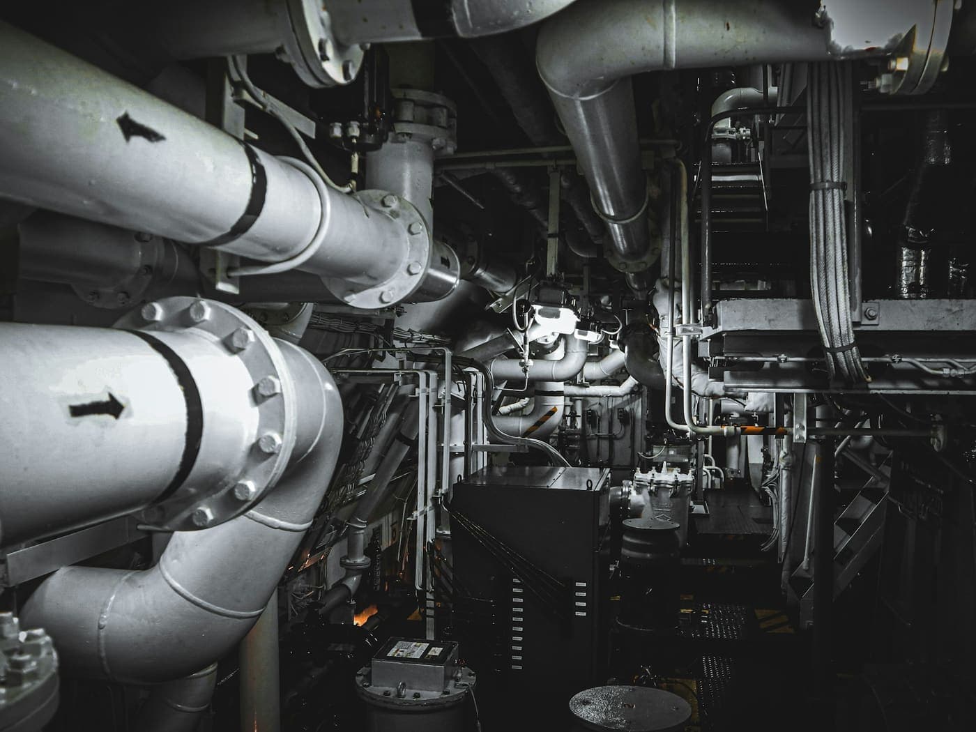 A building services plant room with insulated primary pipework, flow direction arrows and pump sets behind it