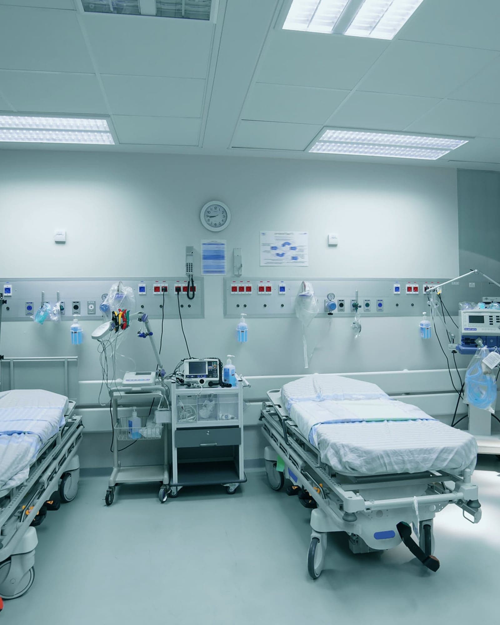 An empty hospital treatment bay with two prepared beds and monitoring equipment along the wall