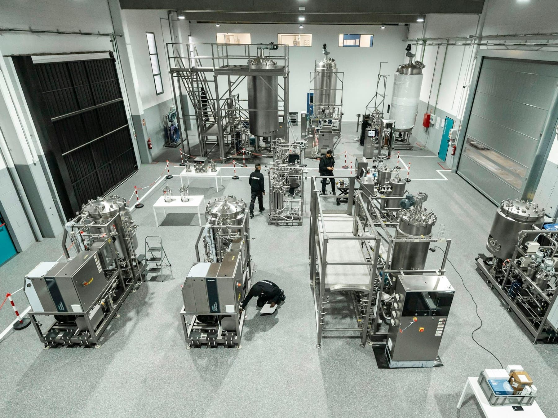 Stainless fermenters and process skids across the floor of a bioprocessing hall