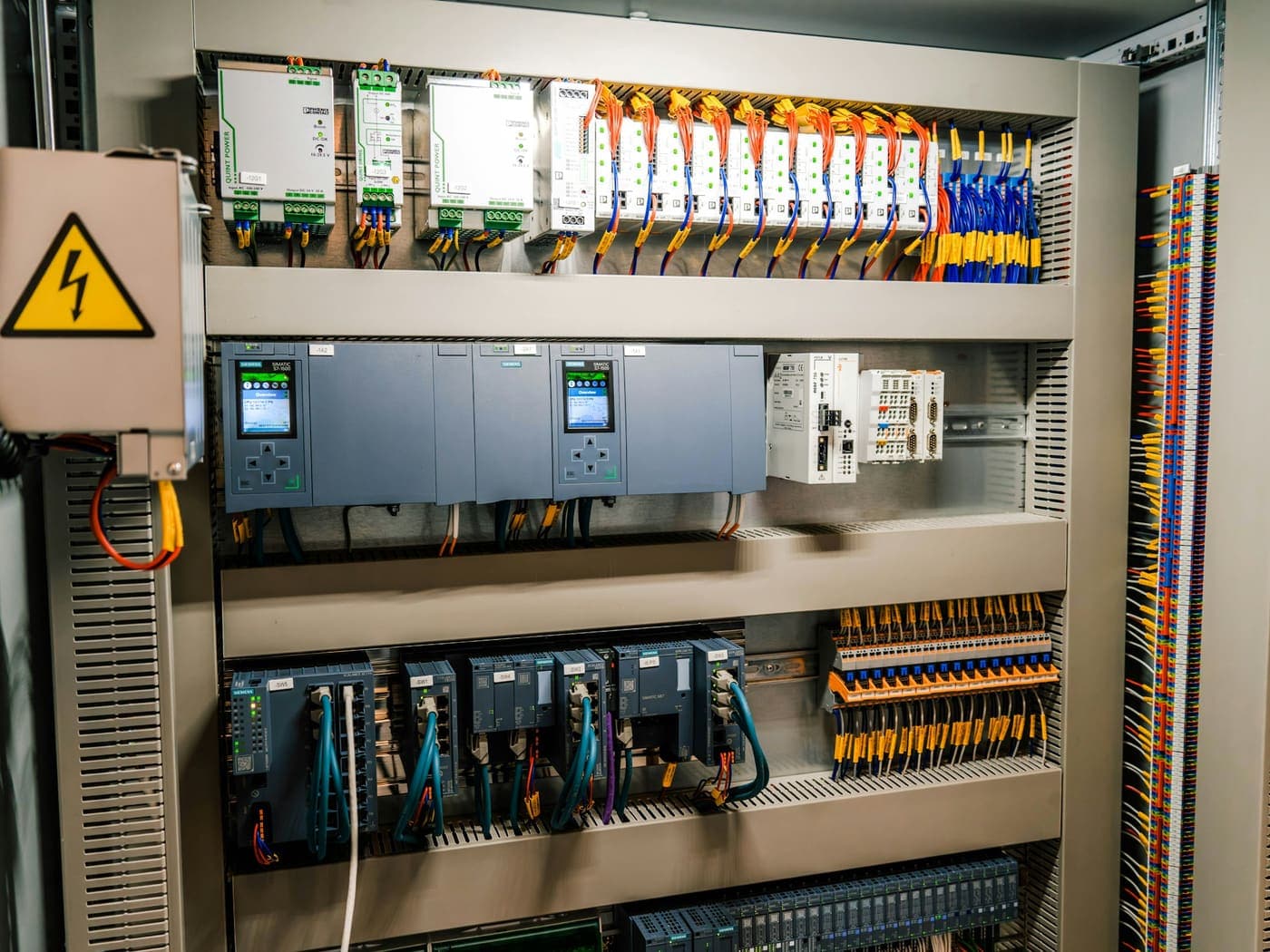 An open industrial control cabinet with its controller modules, terminal rails and wiring looms exposed