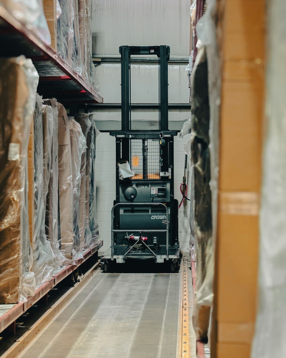 A warehouse aisle of wrapped and palletized finished goods, with an electric stacker working at the far end