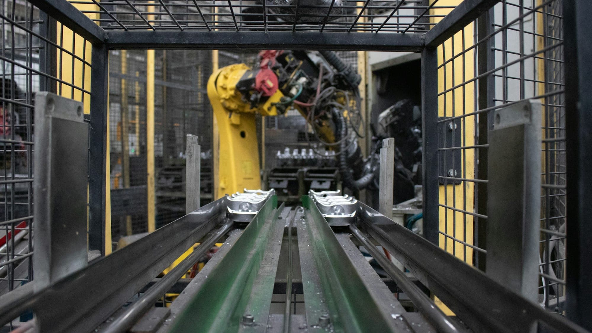 A conveyor running the length of a guarded production cell, with a robot working at the far end of it