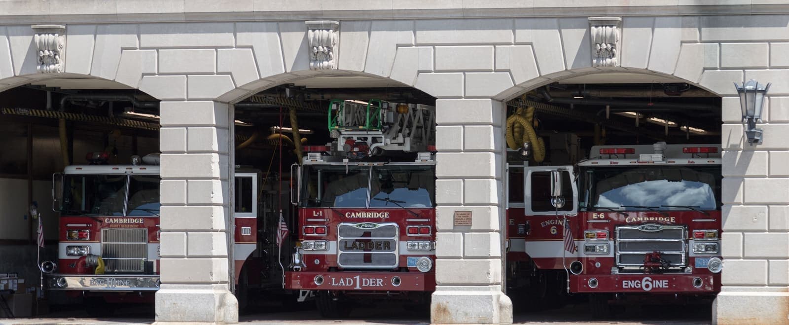 Three fire engines standing in the arched apparatus bays of a city fire station