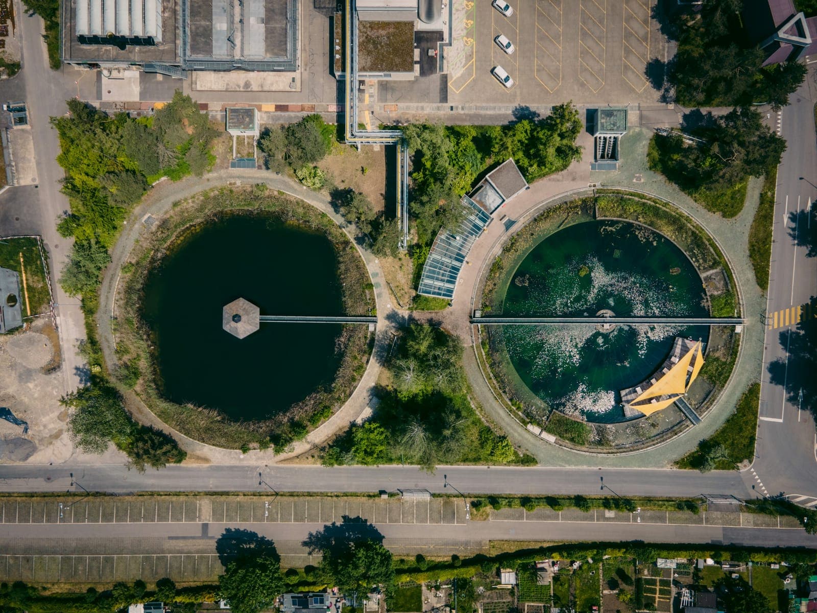 Two circular treatment basins and their plant buildings from above, with the road and housing of the district they serve running along the bottom of the frame
