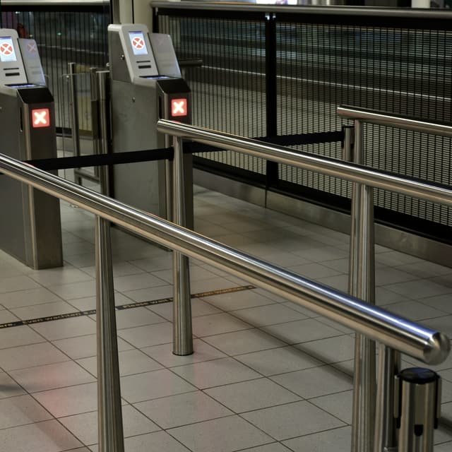 A row of automated access control barriers with card readers on their pedestals, closed across a walkway