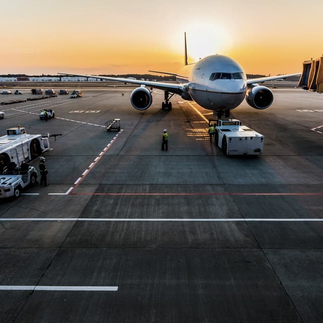 An airliner on stand at sunrise surrounded by ground support equipment, with a loader and tugs alongside it