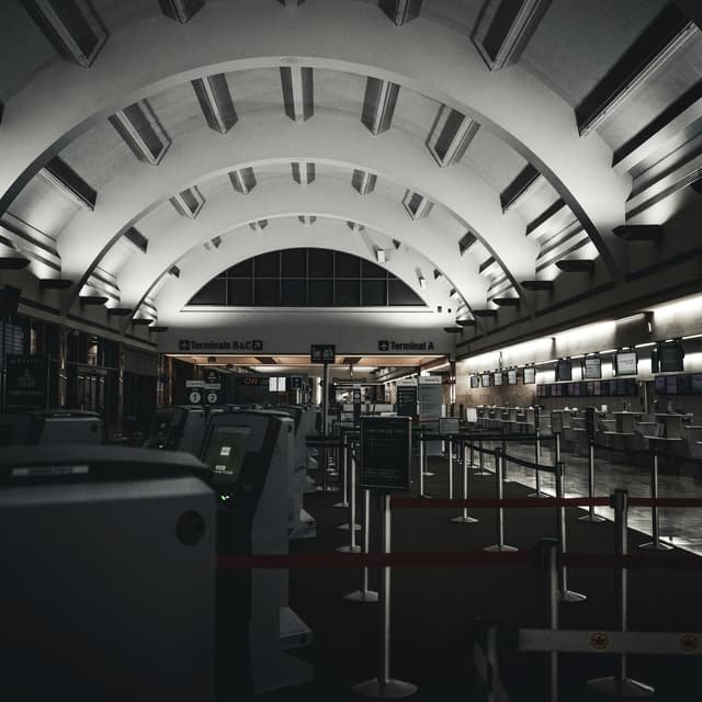 A terminal check in hall under a ribbed vaulted roof, its counters and queue lanes empty